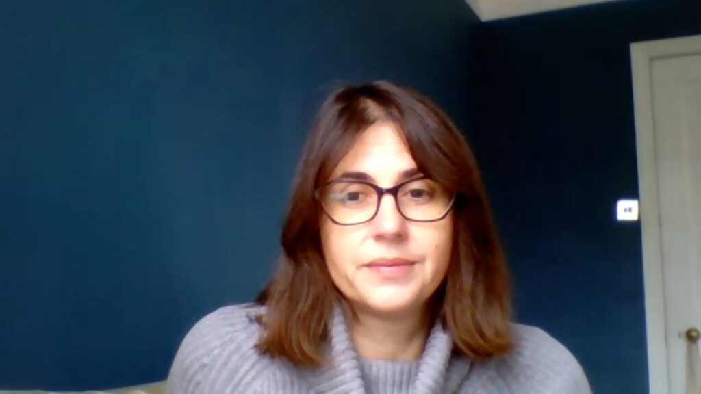 Photo de l’autrice portant des lunettes et un pull gris devant un mur bleu foncé